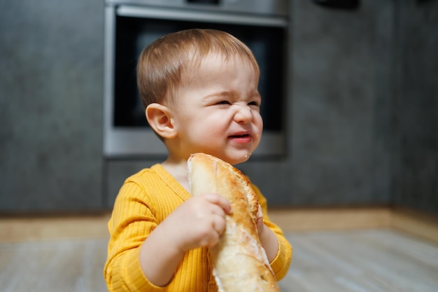 Słodki roczny chłopiec siedzi w kuchni ze świeżym chlebem Dziecko z chlebem na podłodze Dziecko je chleb
