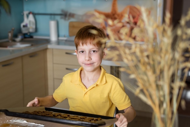 Słodki rudowłosy chłopiec w żółtej koszulce przygotowuje ciasteczka z ciasta w domowej kuchni wesoły facet uśmiecha się Przygotowanie wielkanocnych potraw