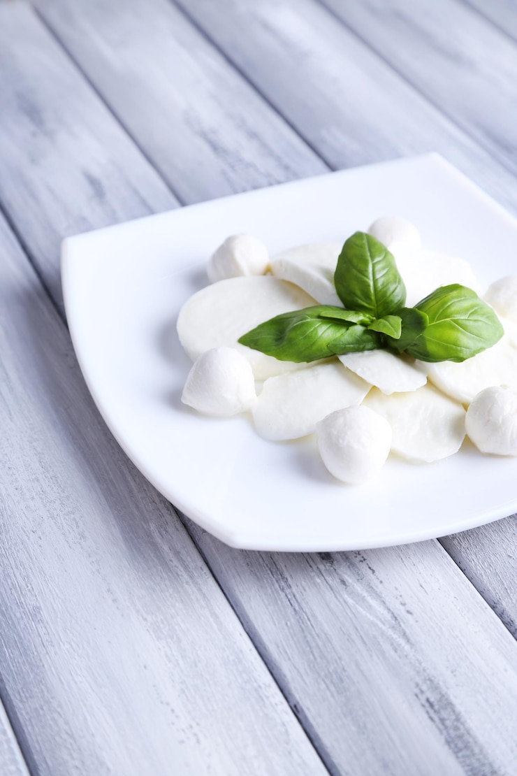 Zdjęcie słodki ser mozzarella z bazylią na talerzu na drewnianym tle
