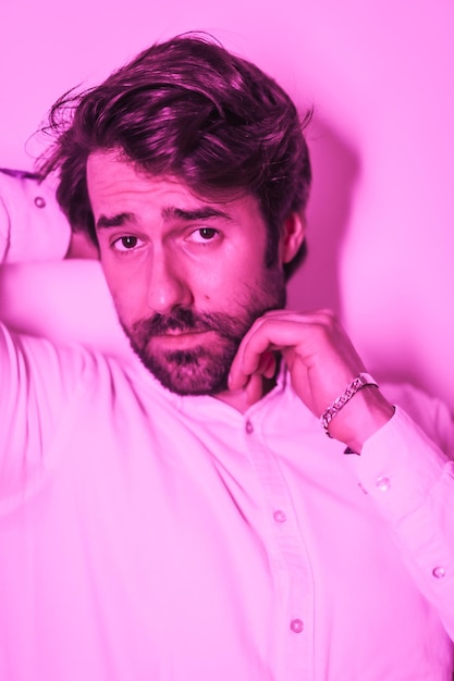 Słodki styl życia studyjnego mężczyzny rasy kaukaskiej w białej koszuli oświetlonej różowym neonowym światłem