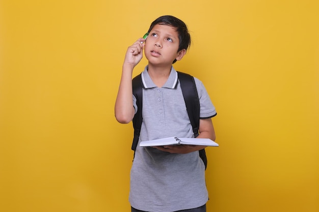 Słodkie azjatyckie dziecko w stylu casual, myślące o czymś, trzymając książkę na żółtym tle Ba