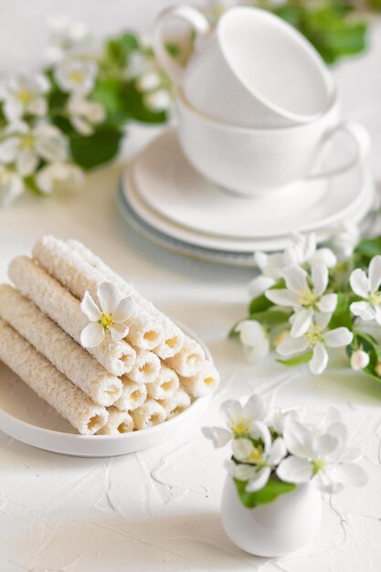 Zdjęcie słodkie ciasteczka z kremem waniliowym na białej talerzu i gruszka z dwoma kubkami herbaty na tle
