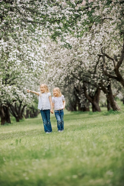 Słodkie dzieci stoją w kwitnącym ogrodzie Dwie siostry spacerują po parku wśród kwitnącego ogrodu