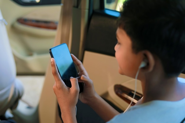 Słodkie dziecko indyjskie siedzi w samochodzie i korzysta z gadżetu smartfona i słuchawek
