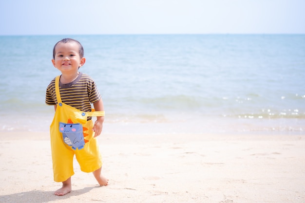 Słodkie dziecko mały chłopiec 15 miesięcy stojący na piaszczystej plaży na wybrzeżu z rozmyciem błękitnego morza