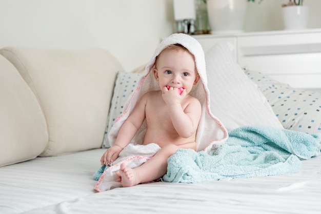 Słodkie dziecko siedzi na łóżku przykrytym ręcznikami i bawi się zabawką