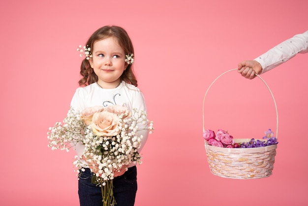 Słodkie dziecko trzyma bukiet wiosennych kwiatów i patrząc na rękę, która trzyma kosz z kwiatami po lewej stronie