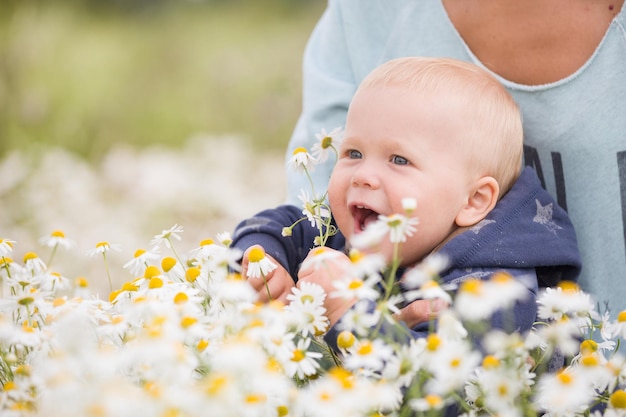 Słodkie dziecko z kwiatami w polu rumianku. Matka trzymająca dziecko i chodząca po łące z dzikimi kwiatami