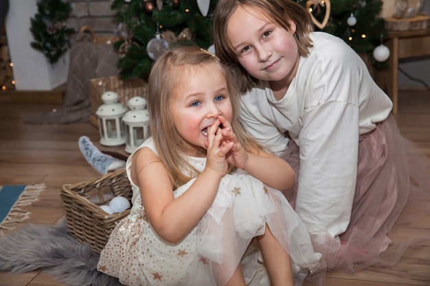 Słodkie dziewczyny siedzą na choince czekając na prezenty, koncepcja noworoczna