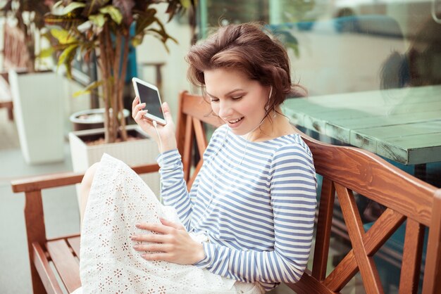 Słodkie hipster kaukaski nastolatka z inteligentny telefon i słuchawki, słuchanie muzyki