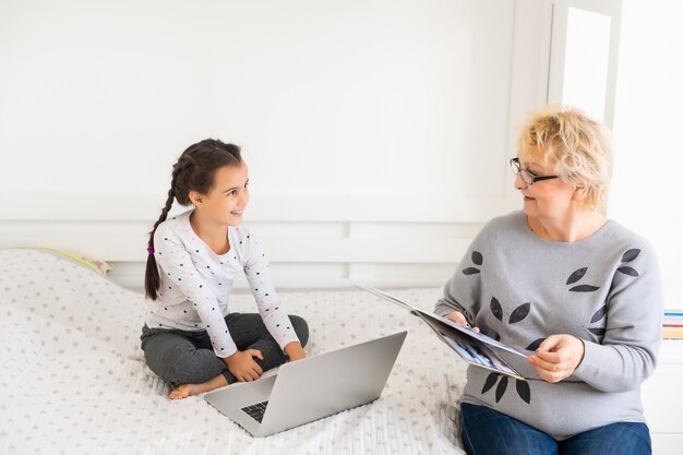 Słodkie I Szczęśliwe Dziecko Dziewczynka Za Pomocą Laptopa Z Babcią, Studiując Przez System E-learningu Online.