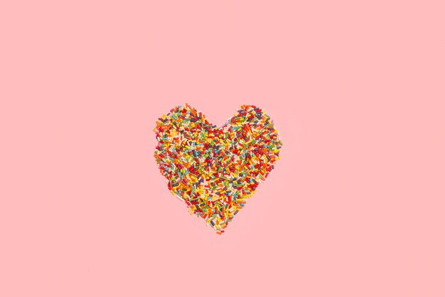 Słodkie kolorowe posypki w kształcie serca na różowym tle z miejsca na kopię