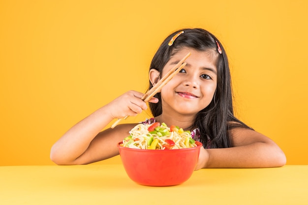 Słodkie małe dziecko dziewczynka indyjski lub azjatycki jedzenie pyszne chińskie makarony z widelcem lub pałeczkami, na białym tle nad kolorowe tło