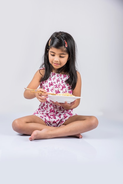 Słodkie małe dziecko dziewczynka indyjski lub azjatycki jedzenie pyszne chińskie makarony z widelcem lub pałeczkami, na białym tle nad kolorowe tło