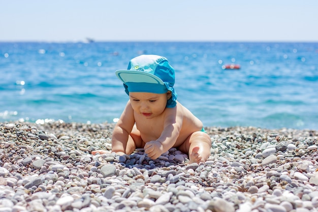 Słodkie pulchne dziecko na kamienistej plaży. Błękitne morze i letnie słońce