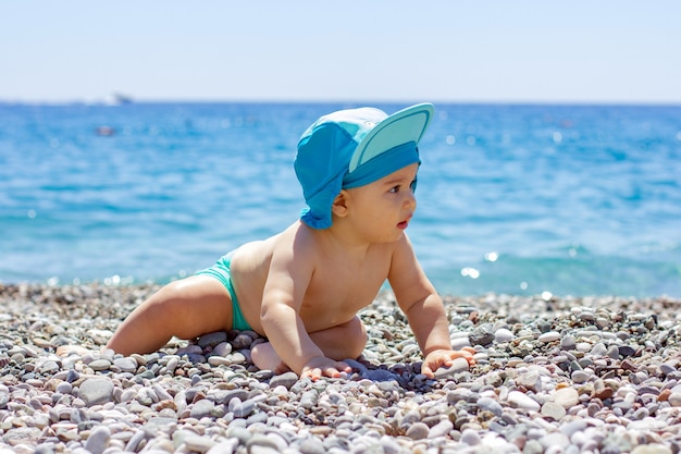 Słodkie pulchne dziecko na kamienistej plaży. Błękitne morze i letnie słońce