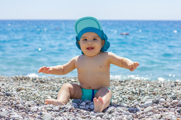 Słodkie pulchne dziecko na kamienistej plaży. Błękitne morze i letnie słońce