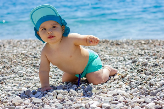 Słodkie pulchne dziecko na kamienistej plaży. Błękitne morze i letnie słońce