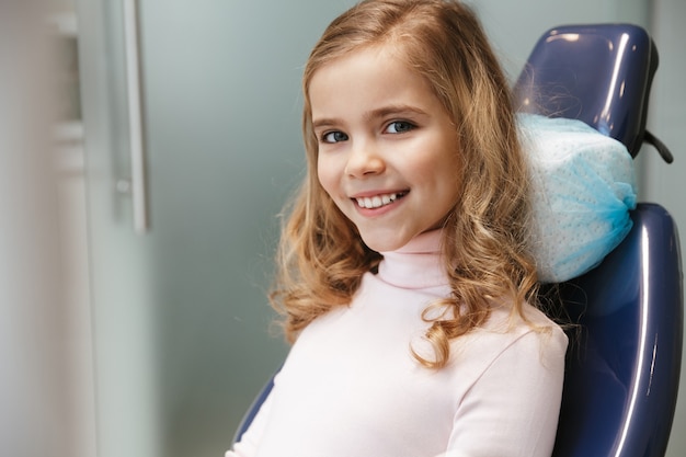 Słodkie Szczęśliwe Piękne Dziecko Dziewczyna Siedzi W Centrum Medycznego Dentysty Patrząc Na Kamery.