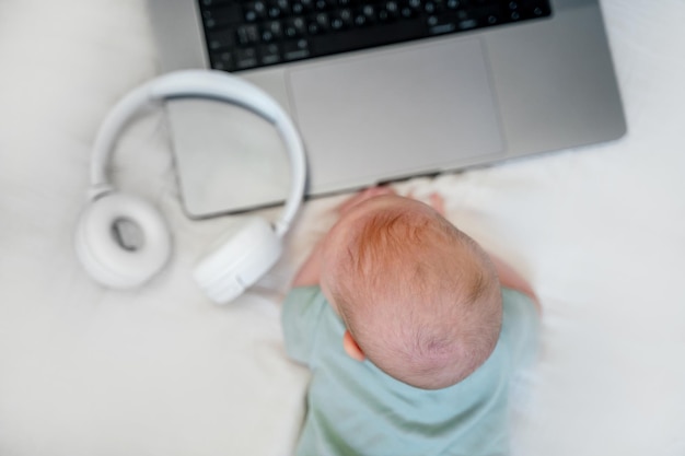 Słodkie trzymiesięczne dziecko leży przed laptopem. Zabawna koncepcja programu biznesowego dla dzieci