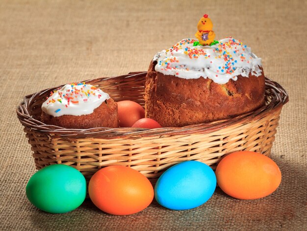 Zdjęcie słodkie wielkanocne ciasta w wiklinowym koszu i kolorowe pisanki z worem na powierzchni