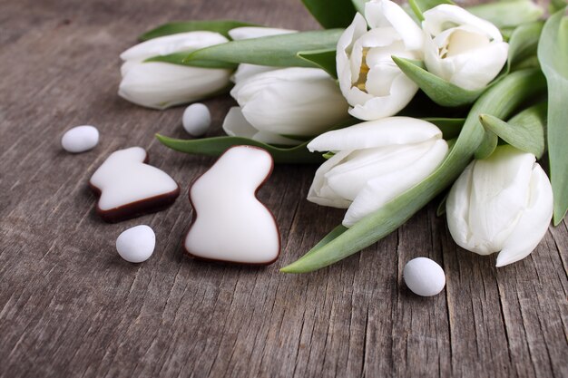 Słodycze na Święta Wielkanocne. Białe tulipany, czekoladowe jajka i królik. Stare drewniane tła.