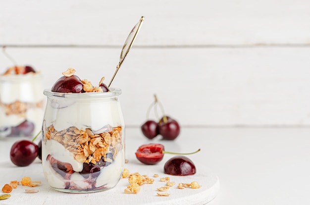 Słoik muesli z jogurtem greckim i czereśniami na białym drewnianym