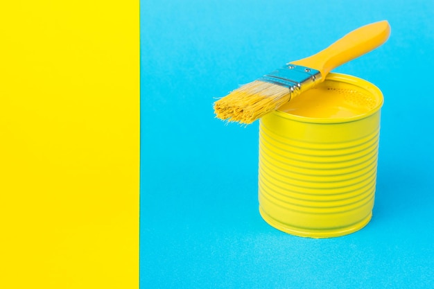 Słoik z jasnożółtą farbą i pędzlem na niebieskim tle oraz żółtym paskiem papieru Modne kolory Minimalna koncepcja wyboru wnętrza
