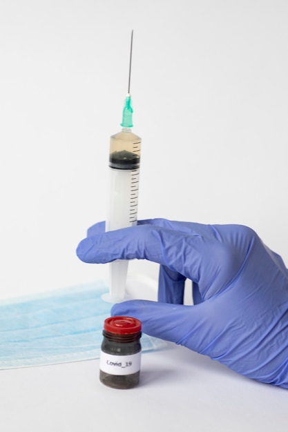 Słoik z lekarstwem na koronawirusa stoi naprzeciw dłoni w rękawiczce trzymającej strzykawkę ze szczepionką. Medecina, COVID-19 Naukowcy wynaleźli szczepionkę.