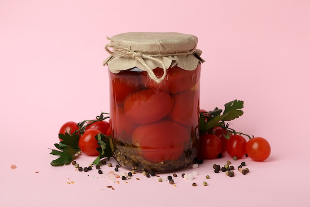 Słoik z marynowanymi pomidorami i składnikami na różowym tle