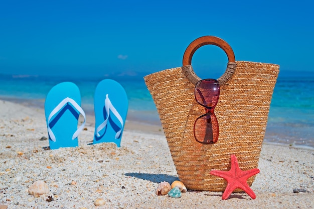 Słomiana torba przy brzegu z niebieskimi sandałami w tle