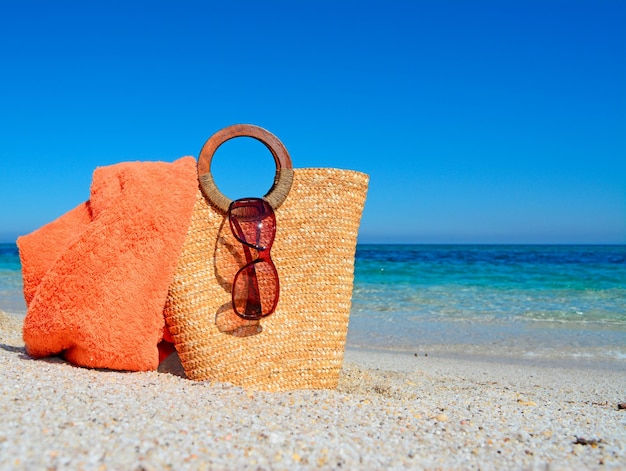 Zdjęcie słomiana torba z okularami przeciwsłonecznymi i ręcznikiem plażowym przy tropikalnym brzegu