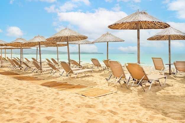 Słomiane parasole i leżaki na słonecznym złotym brzegu morza