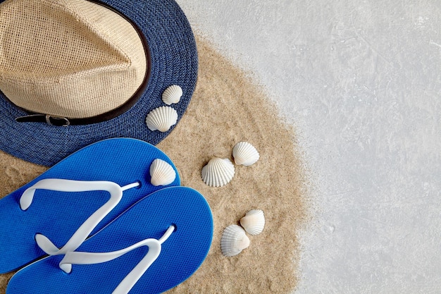 Słomkowy kapelusz klapki i muszle na rozproszonym piasku morskim na jasnoszarym betonowym tle Koncepcja wakacji na plaży Widok z góry z kopią