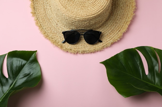 Słomkowy kapelusz, liście palmowe i okulary przeciwsłoneczne na różowym tle na białym tle