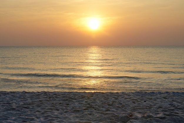 Słońce na niebie z morzem i piaskiem na plaży z ciepłym pomarańczowym światłem