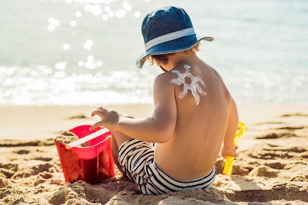 Słońce rysujące balsam do opalania z filtrem przeciwsłonecznym na plecach chłopca kaukaskie dziecko siedzi z plastikiem