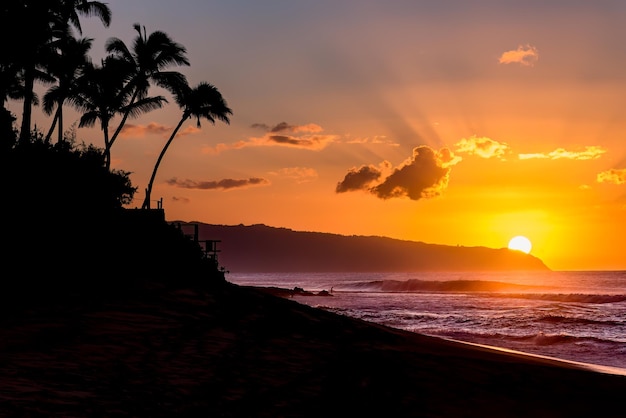 Słońce za górą nad falami i palmami na Sunset Beach na Hawajach