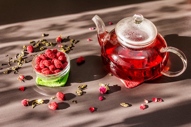 Zdjęcie słoneczne poranne śniadanie. słodka malinowa zielona herbata w szklanym czajniku z suszonymi owocami, kwiatami i liśćmi