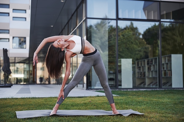 Słoneczny letni poranek. Młoda kobieta lekkoatletycznego robi handstand na ulicy parku miejskiego wśród nowoczesnych budynków miejskich. Ćwicz na świeżym powietrzu zdrowy styl życia.