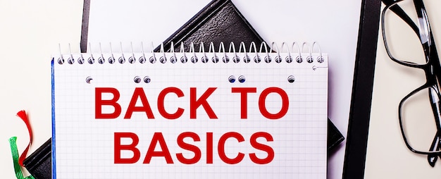 Słowa Back To Basics Są Zapisane Na Czerwono W Białym Notesie Obok Okularów W Czarnych Oprawkach.