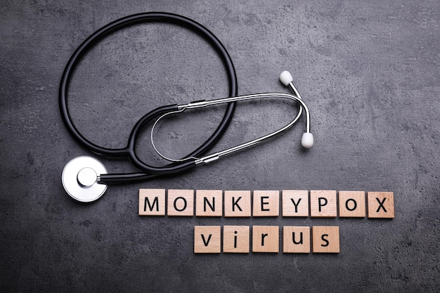 Zdjęcie słowa monkeypox virus wykonane z drewnianych kwadratów i stetoskopu na szarym stole leżały płasko