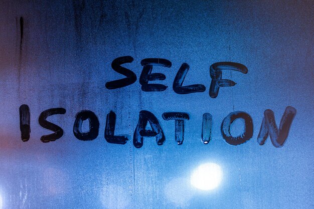 Słowa samoizolacja napisane odręcznie na mokrym szkle w nocy zbliżenie pełnoklatkowy obraz z selektywną ostrością