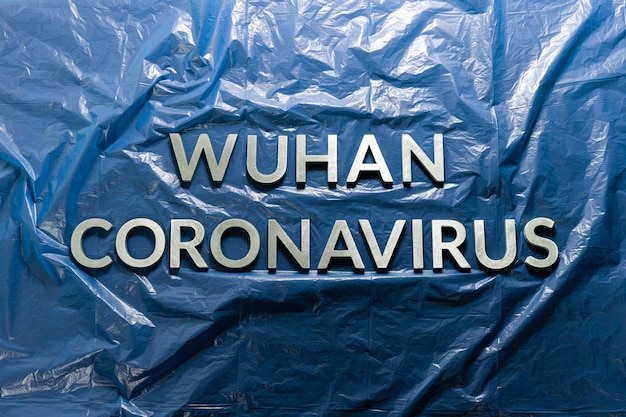 Słowa wuhan coronavirus ułożone metalowymi literami na zmiętym niebieskim tle folii z tworzywa sztucznego płasko ułożone z kompozycją