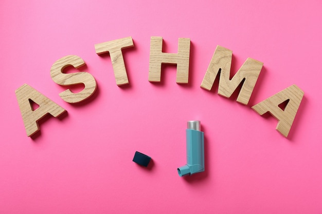 Słowo Astma z drewnianych liter i inhalatora na różowym tle