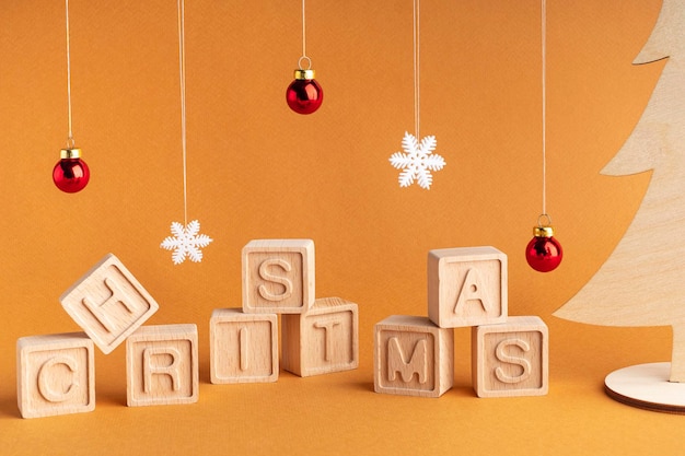 Słowo Boże Narodzenie składa się z drewnianych kostek na pomarańczowym tle Płatki śniegu i bombki Kartka świąteczna