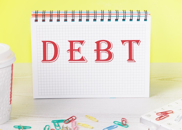Słowo dług jest zapisane na pustej kartce w notatniku stojącym na stole na żółtym tle