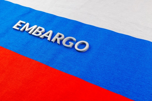 Słowo embargo nałożone srebrnymi metalowymi literami na rosyjskiej trójkolorowej fladze w widoku ukośnym