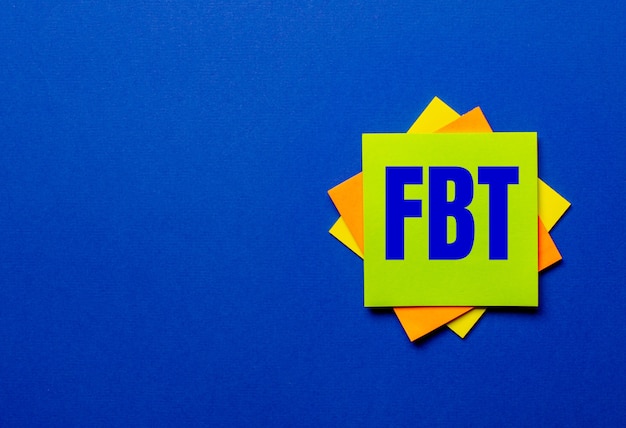 Słowo FBT Fringe Benefit Tax jest napisane na jasnych naklejkach na niebieskim tle