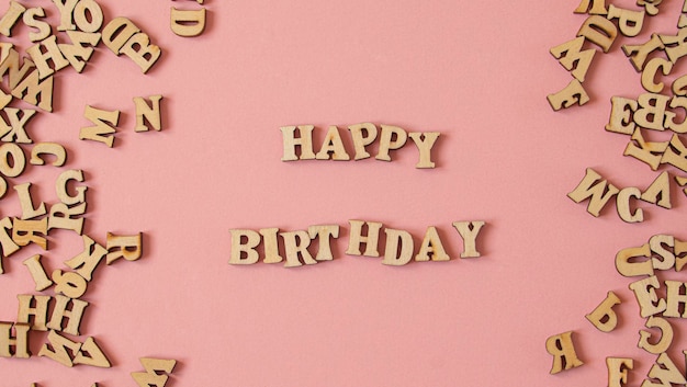 Słowo „Happy Birthday” napisane w języku angielskim drewnianymi literami na różowym tle